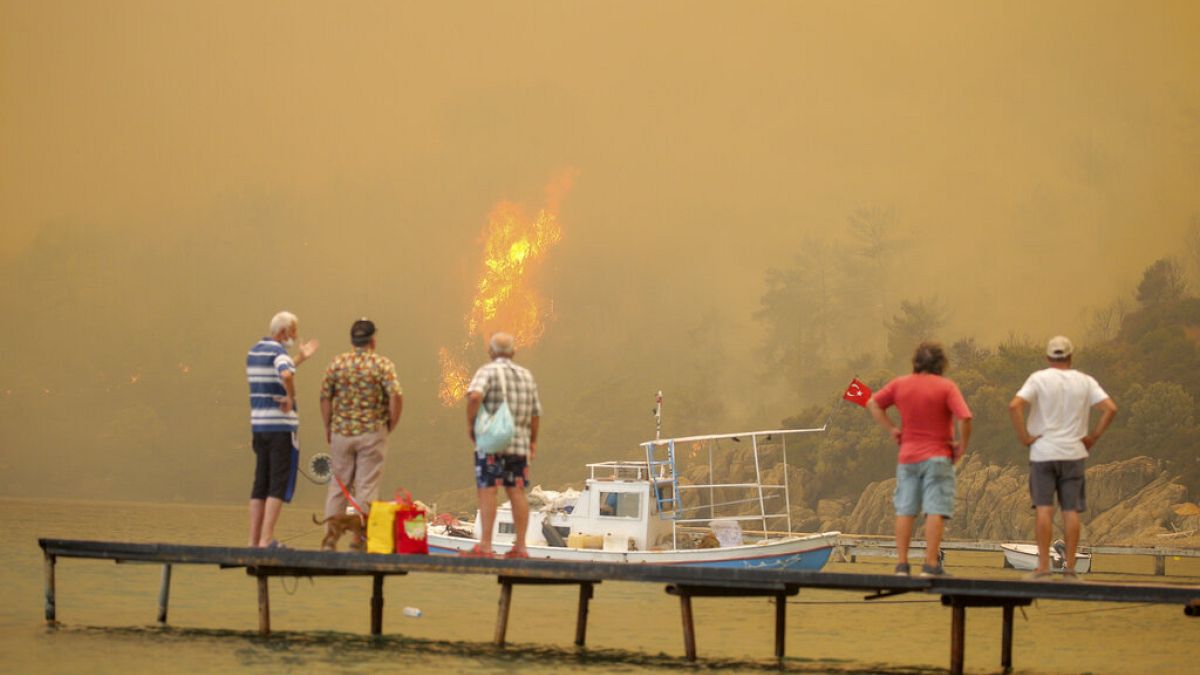 A strandtól méterekre tomboló tüzet nézik egy stégről turisták a törökországi Bodrumnál