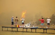 A strandtól méterekre tomboló tüzet nézik egy stégről turisták a törökországi Bodrumnál