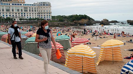 People wearing face masks to protect against COVID-19 walk past a beach in Biarritz, southwestern France, July 28, 2021.