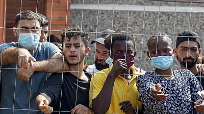 Migrants wait to buy some things standing behind the fence at the refugee camp in the village of Verebiejai
