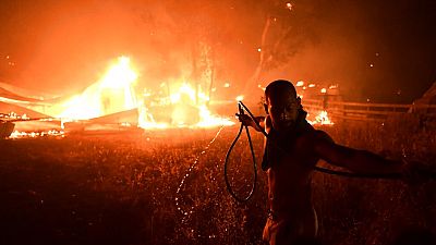 A man uses a water hose during a wildfire in Adames area, in northern Athens, Greece, Tuesday, Aug. 3, 2021