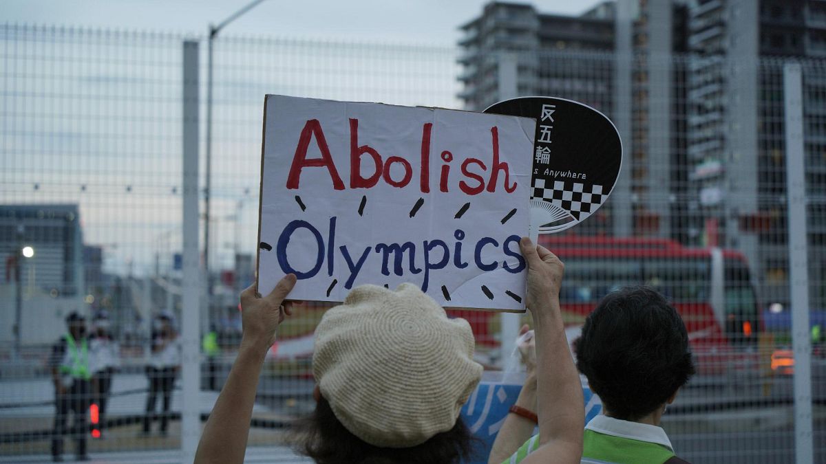 متظاهرون مناهضون للأولمبياد يحملون لافتات أمام السياج حول القرية الرياضية للألعاب الأولمبية الصيفية في طوكيو، اليابان، الجمعة 30 يوليو 2021
