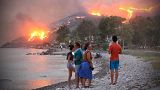 People on a beach watch the blazes spreading up a hill in the Aegean coast city of Oren, near Milas, in the holiday region of Mugla.