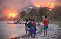 People on a beach watch the blazes spreading up a hill in the Aegean coast city of Oren, near Milas, in the holiday region of Mugla.