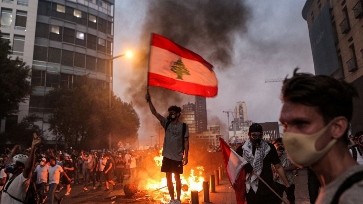 A protester stands with a Lebanese national flag during clashes with army and security forces near the Lebanese parliament headquarters in Beirut on August 4, 2021.  