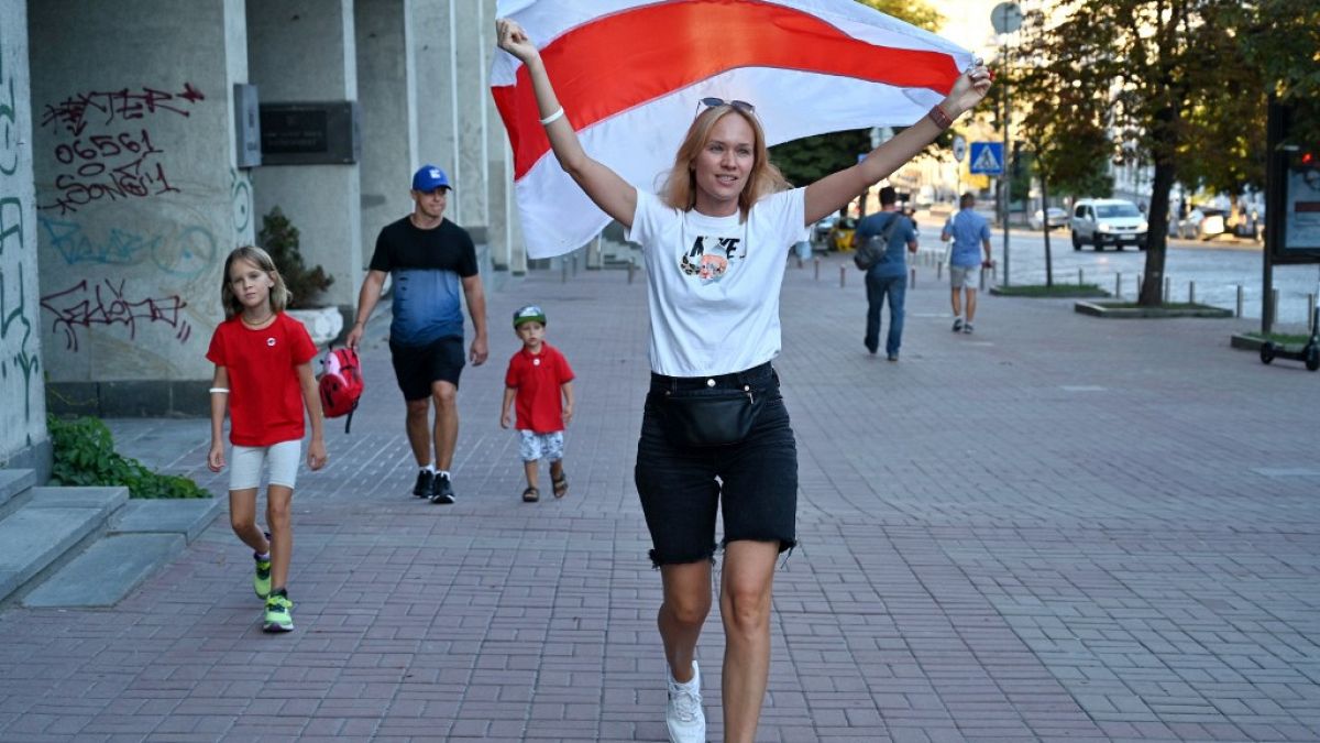A member of the Belarusian diaspora in Ukraine, holds up a former national flag of Belarus as she and her family walks in Kiev during a rally outside Belarus embassy