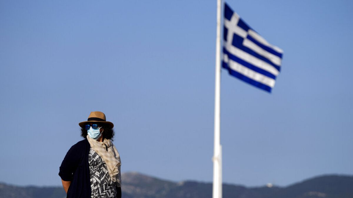 Εργαζόμενη στον αρχαιολογικό χώρο με μάσκα δίπλα στην ελληνική σημαία στον βράχο της Ακρόπολης
