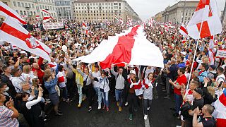 August 2020, demonstrators carry a huge historical flag of Belarus as thousands gather for a protest at the Independence square in Minsk, Belarus.