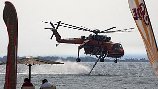 Un helicóptero contraincendios recoge agua del mar ante la mirada de los bañistas en Pefki, en la isla de Eubea.