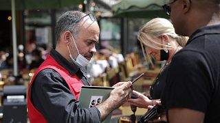 A waiter checks diners' health passes at a restaurant in Paris, 9 August 2021.
