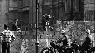 This picture taken in August 1961 shows police officers watch workers lay bricks on the other side of the so called Berlin Wall in the street Bernauer Strasse in Berlin.