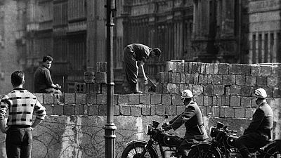 This picture taken in August 1961 shows police officers watch workers lay bricks on the other side of the so called Berlin Wall in the street Bernauer Strasse in Berlin.