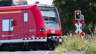 A Deutsche Bahn (DB) commuter train passes a level crossing with a red light in Roessing, Germany, Aug. 11, 2021.