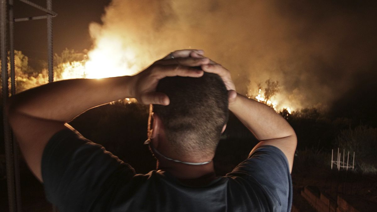 رجل ينظر إلى حريق غابة بالقرب من قرية الأربعاء ناث إراثن  بتيزي وزو في منطقة القبائل في الجزائر.
