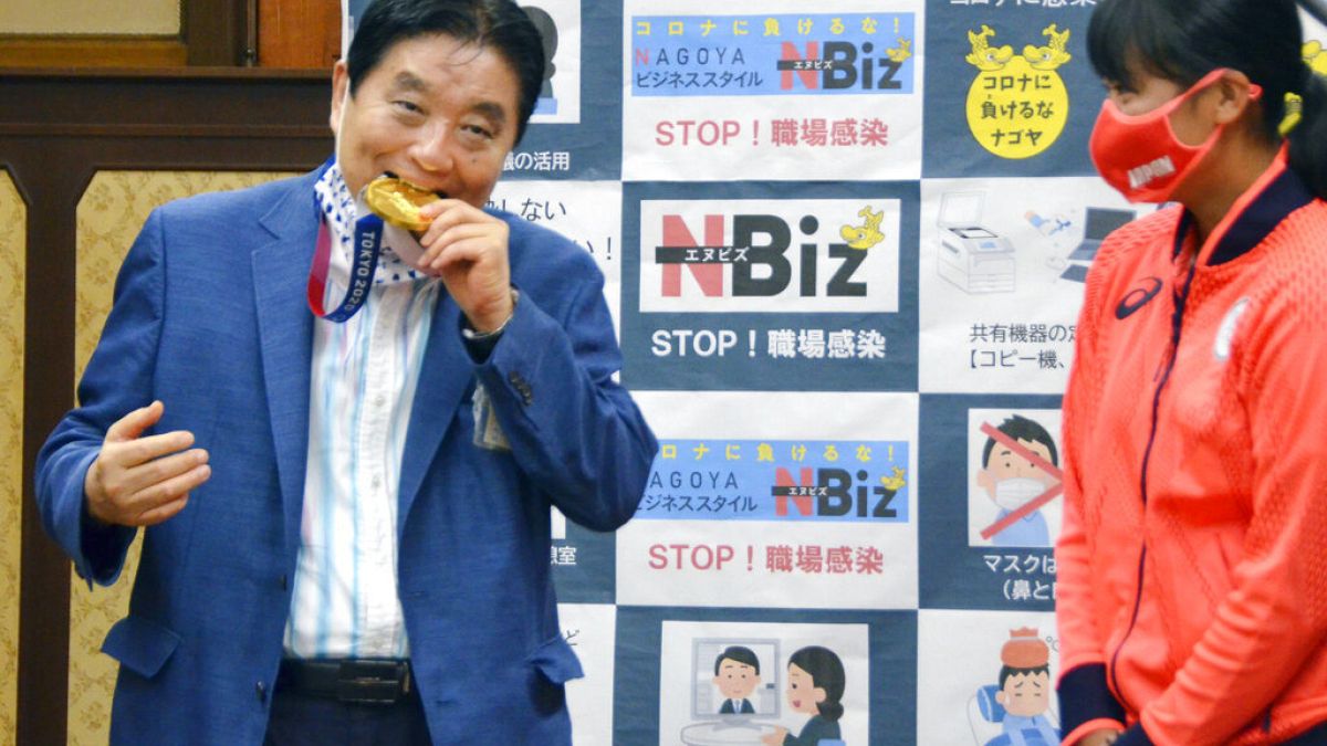 4 agosto 2021: il sindaco di Nagoya Takashi Kawamura, a sinistra, morde la medaglia d'oro olimpica di Miu Goto, a destra, dalla squadra di softball giapponese,