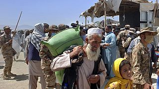 Pakistani soldiers stand guard while stranded people walk towards the Afghan side at a border crossing point, in Chaman, Pakistan, Friday, Aug. 13, 2021