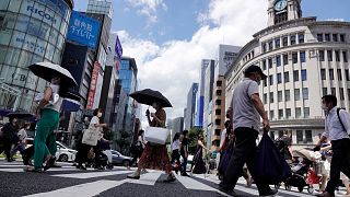 FILE - In this Aug. 10, 2021, file photo, people wearing face masks to help curb the spread of the coronavirus walk under the scorching sun in the Ginza Shopping district.