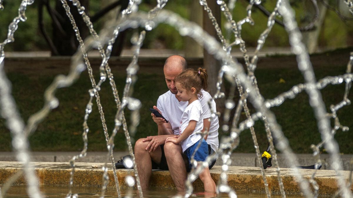 Un padre y su hija se refrescan en una fuente de Madrid, España
