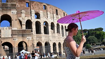 A woman shields from the sun under an umbrella outside the Colosseum in Rome.