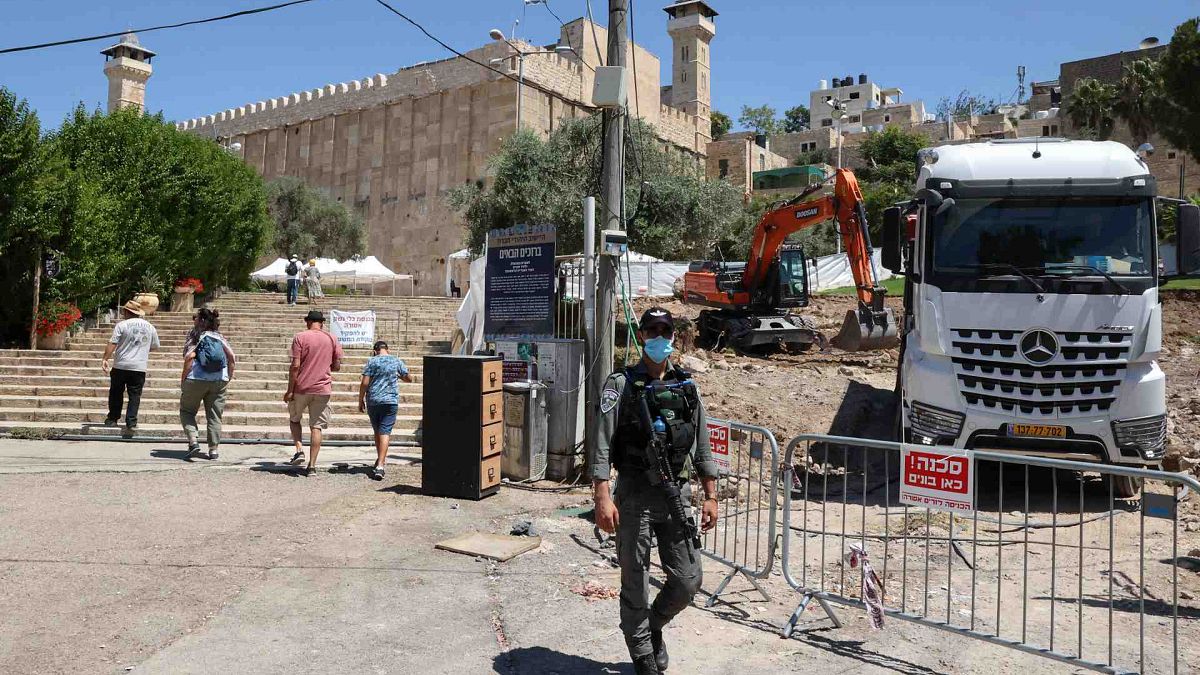 ضابط أمن إسرائيلي يقف حارسا أثناء قيام حفارة بأعمال البناء بجوار المسجد الإبراهيمي في مدينة الخليل المقسمة في الضفة الغربية المحتلة، 15 أغسطس 2021