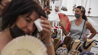Mujeres se refrescan con abanicos en el mercadillo del Rastro durante una ola de calor en Madrid, España, el 15 de agosto de 2021