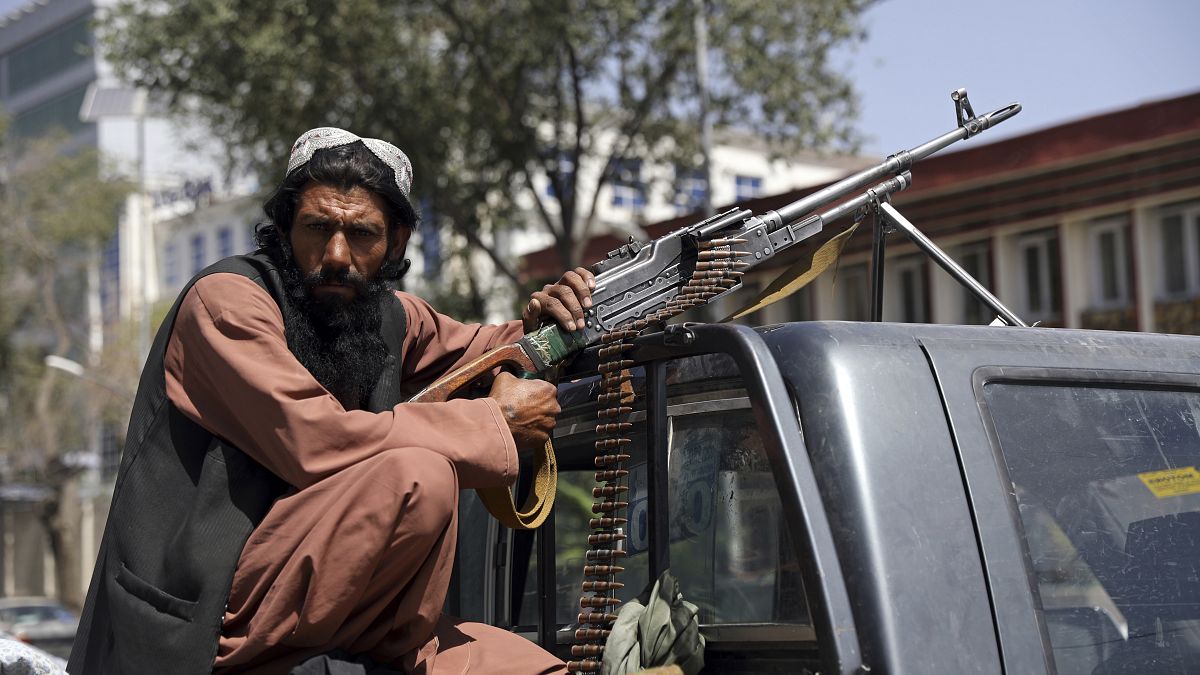A Taliban fighter sits on the back of a vehicle with a machine gun in front of the main gate leading to the Afghan presidential palace, in Kabul, Afghanistan.