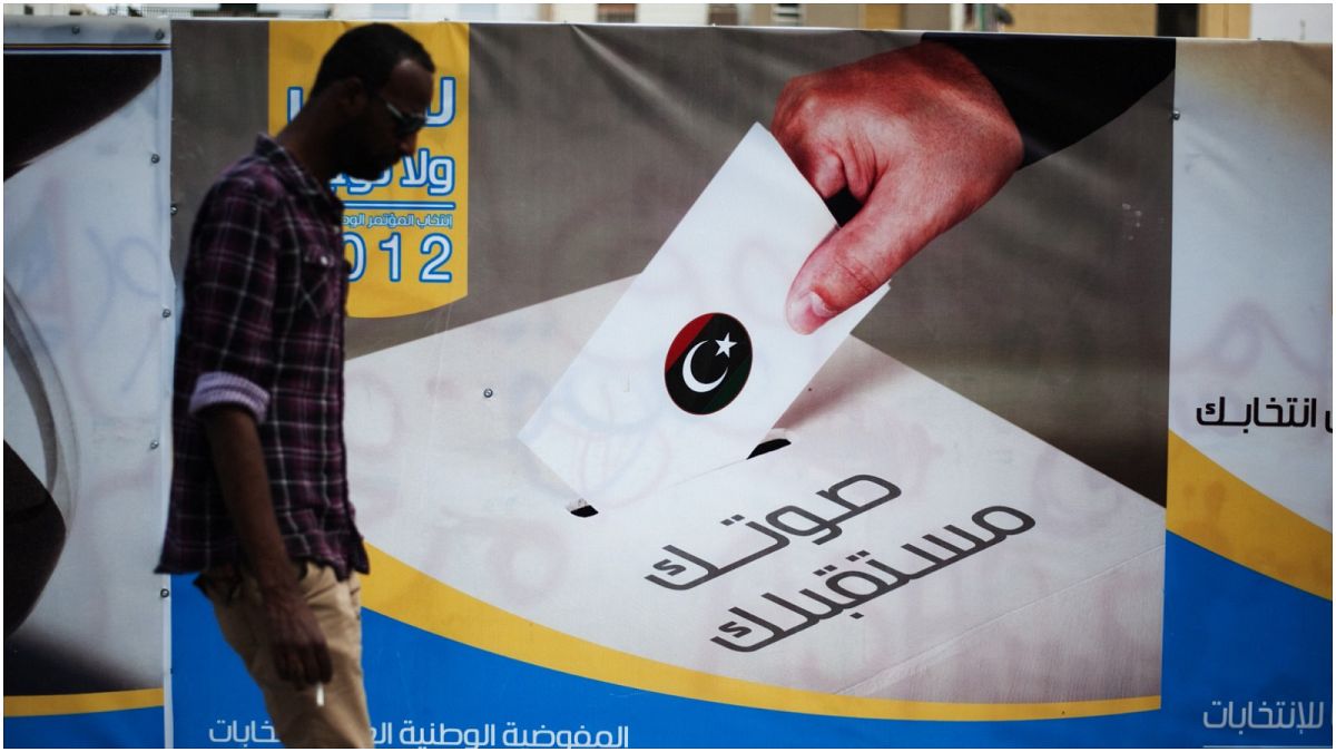 صورة أرشيفية لرجل ليبي يمر من أمام لوحة إعلانات للمفوضية العليا للانتخابات في 19 أيار/مايو 2012 في طرابلس