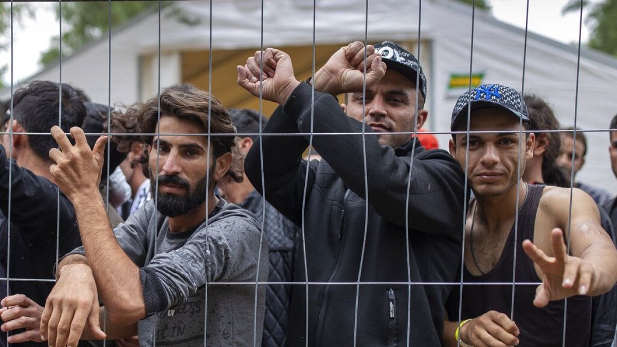 Migrants stand behind a fence inside the newly built refugee camp in the Rudninkai military training ground, some 38km (23,6 miles) south from Vilnius