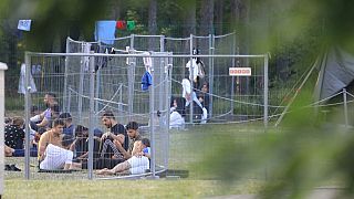 Migrants are seen through fences as they sit on the ground in a camp near the border town of Kapciamiestis, Lithuania.