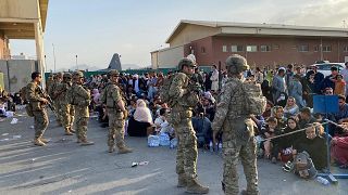 جنود أمريكيون يقفون للحراسة بينما ينتظر الأفغان ركوب طائرة عسكرية أمريكية لمغادرة أفغانستان، في المطار العسكري في كابول في 19 أغسطس 2021