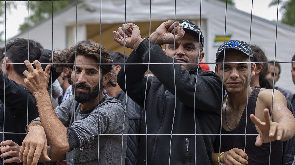 In this file photo taken on Wednesday, Aug. 4, 2021, migrants stand behind a fence inside a Lithuanian refugee camp near the Belarusian border.