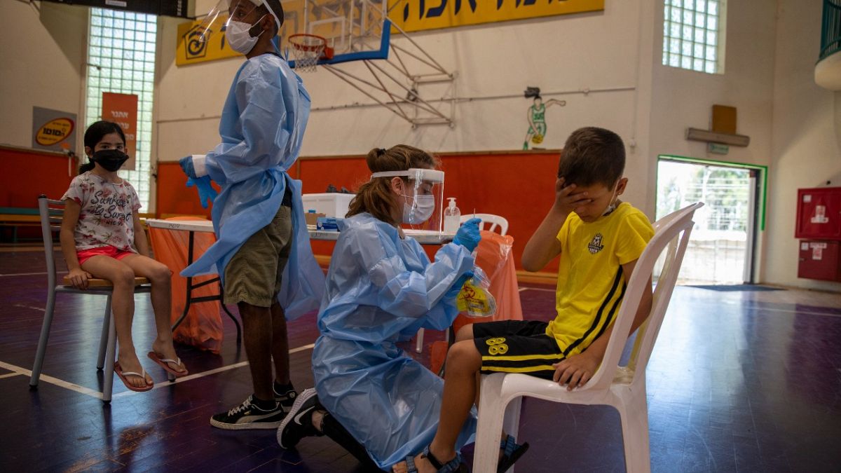 طاقم طبي يختبر الأطفال الإسرائيليين في ملعب لكرة السلة تحول إلى مركز لفحص فيروس كورونا في إسرائيل.