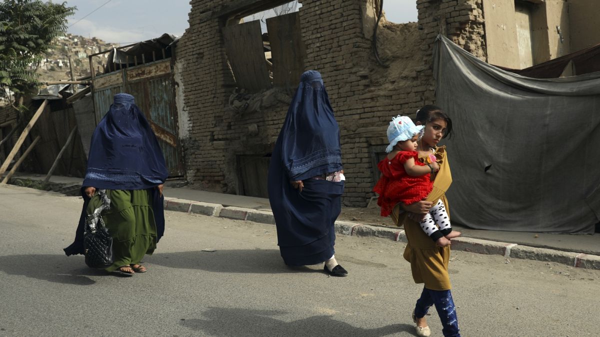 Burkába öltözött nők és gyerekek sétálnak egy kabuli utcán