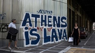 Pedestrians walk past grafitti “Athens is Lava” in central Athens on July 12, 2017.