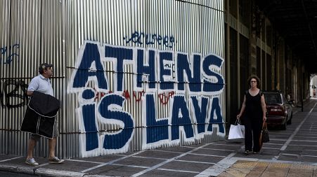Pedestrians walk past grafitti “Athens is Lava” in central Athens on July 12, 2017.