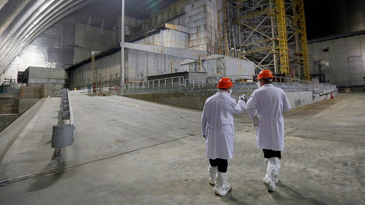 Des employés devant l'ancien réacteur de la centrale nucléaire de Tchernobyl recouvert d'un abri récent, le 15 avril 2021