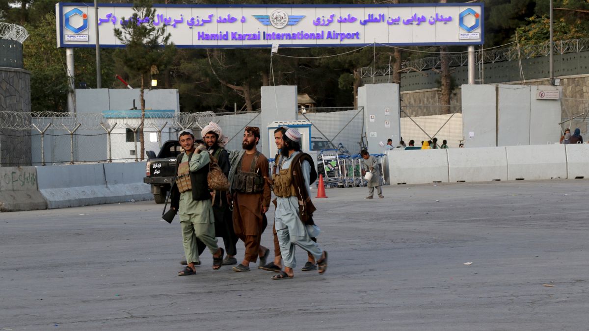 مقاتلو طالبان يسيرون أمام بوابة مطار حامد كرزاي الدولي في كابول ، أفغانستان.