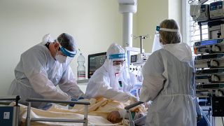 Védőfelszerelést viselő orvos és ápolók egy oxigénellátást segítő helmet sisakot helyeznek fel egy betegre 