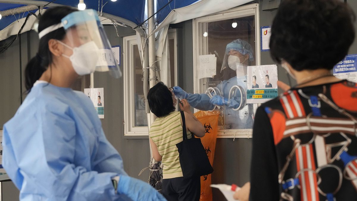 A medical worker in a booth takes a nasal sample from a woman during coronavirus testing at a makeshift testing site in Seoul