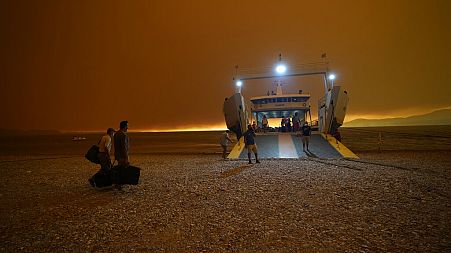 Smoke spreads over the sea as local residents and tourists use a ferry to evacuate Pefki village on Evia island on August 8 2021.