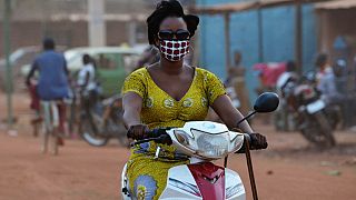 A woman wears a mask as she rides a motorbike in the streets of Ouagadougou.