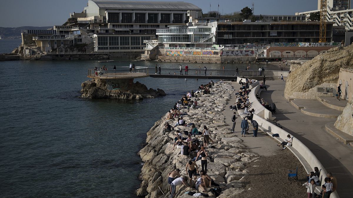 Sunbathers sit by the Plage des Catalans in Marseille, southern France, Friday, April 2, 2021.