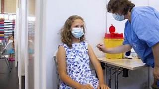 A medical worker administers a shot of a coronavirus vaccine to a 13-year-old girl at a vaccination center inside a sports hall in Estonia's second-largest city, Tartu.