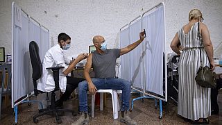An Israeli man takes a selfie while receiving the third Pfizer-BioNTech COVID-19 vaccine from medical staff at a coronavirus vaccination center in Ramat Gan, Israel.