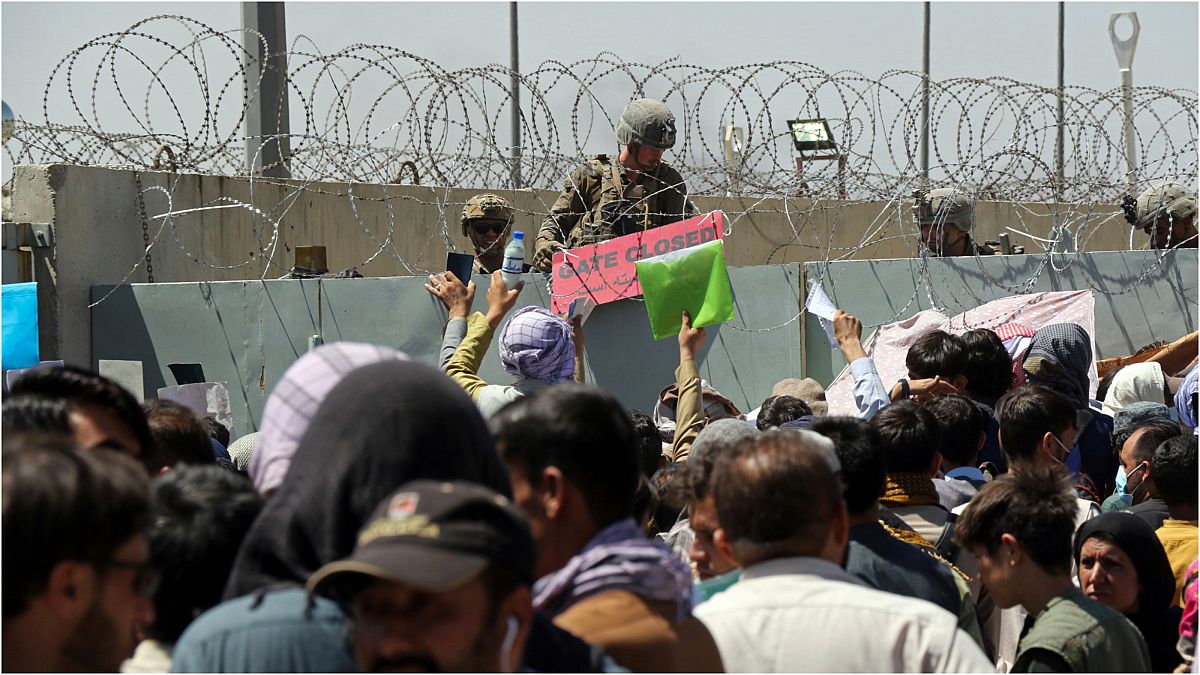 جندي أمريكي يقف خلف الأسلاك الشائكة لجدار مطار كابول وأمام مواطنون أفغان يريدون مغادرة البلاد بعد سيطرة حركة طالبان على بلادهم