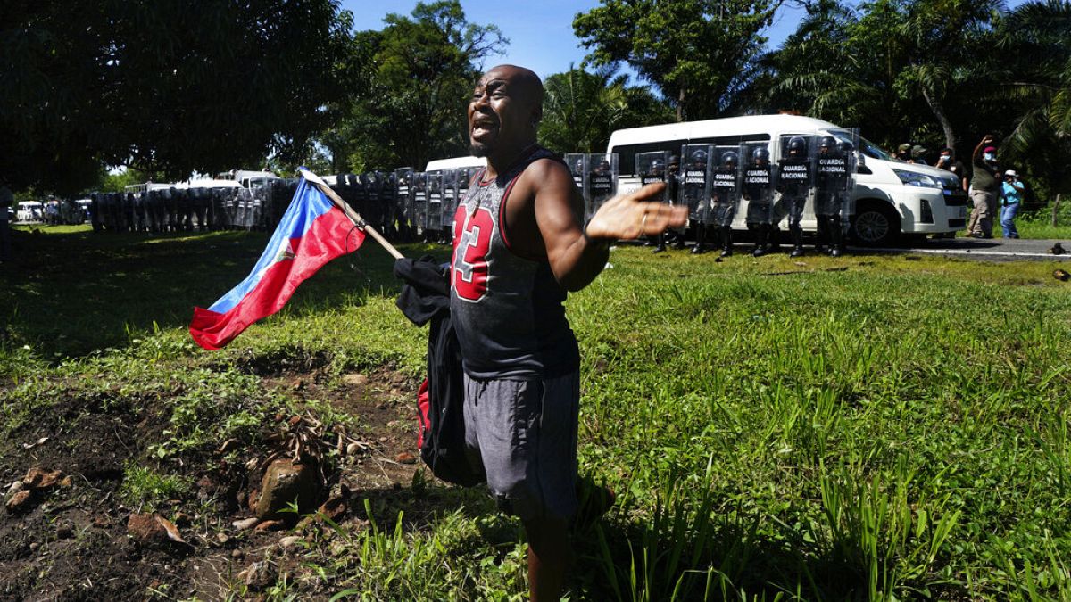Un migrante haitiano suplica a las fuerzas mexicanas que no le detengan mientras sostiene una bandera de su país
