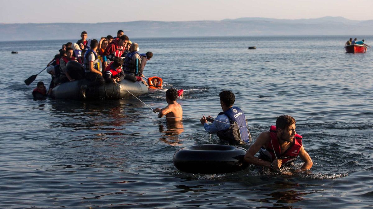 مهاجرون يسحبون زورقًا مكتظًا باللاجئين السوريين والأفغان الذين يصلون من السواحل التركية إلى جزيرة ليسبوس اليونانية، الإثنين، 27 يوليو/تموز 2015