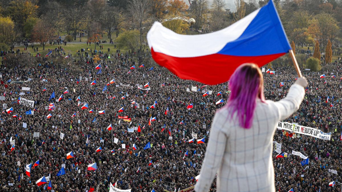 A woman waves a Czech flag from a roof as people take part in a large anti-government protest in Prague, Czech Republic, Saturday, Nov. 16, 2019