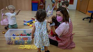 A teacher wearing a face mask to protect against the spread of coronavirus reacts with children in a class, at Vallehermoso school