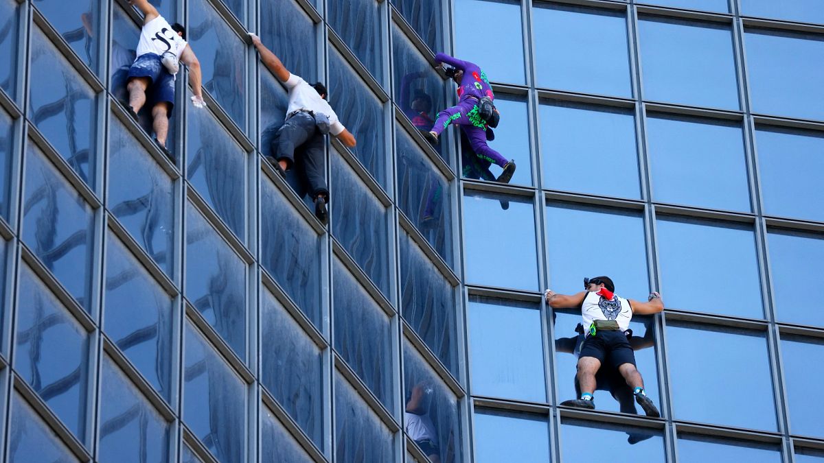 French urban climber Alain Robert (2R), popularly known as the "French Spiderman" climbs  the Total tower in La Defense near Paris, on September 7, 2021. 